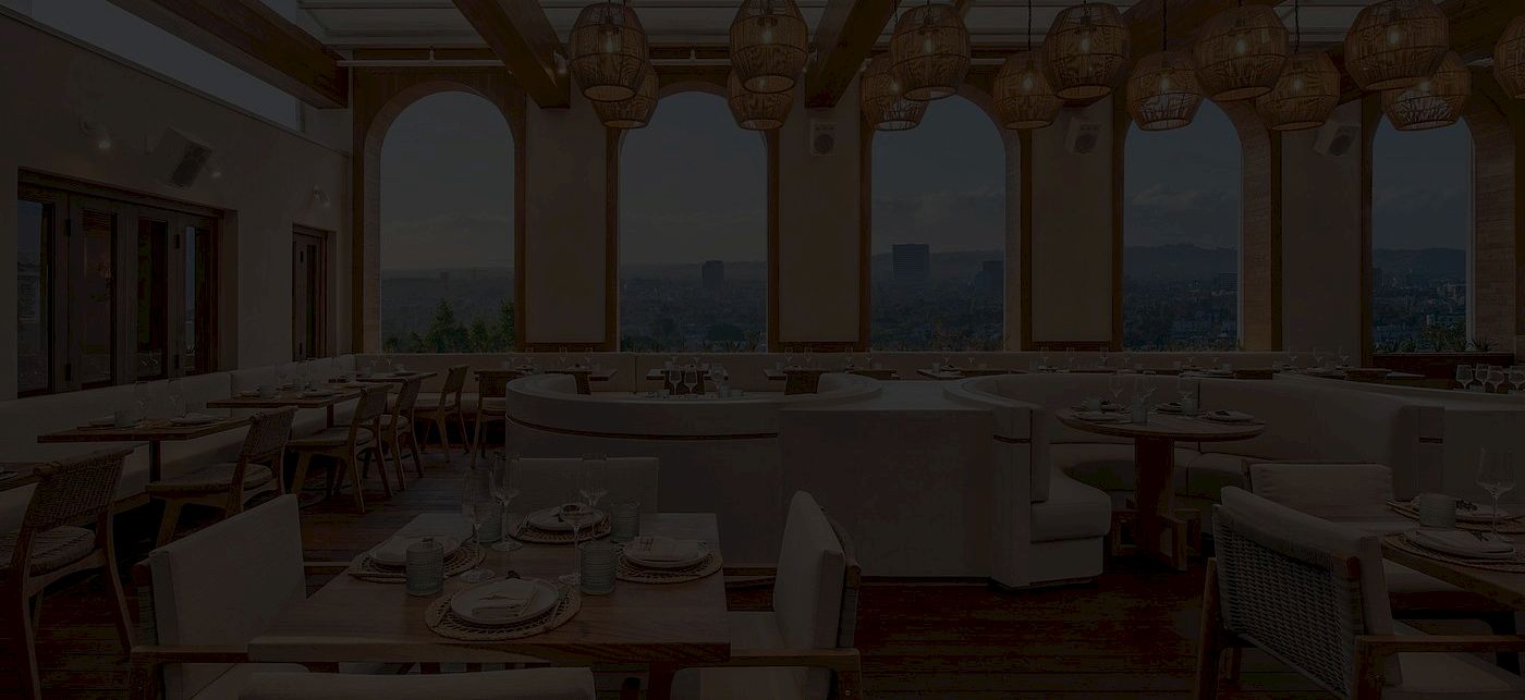 A cozy, dimly lit restaurant with arched windows, hanging lanterns, and neatly set tables and chairs for a meal, overlooking a view.