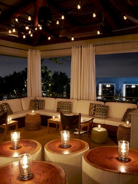 A cozy rooftop lounge with circular beige couches, wooden tables, and softly lit candles creating a warm, intimate ambiance at night.