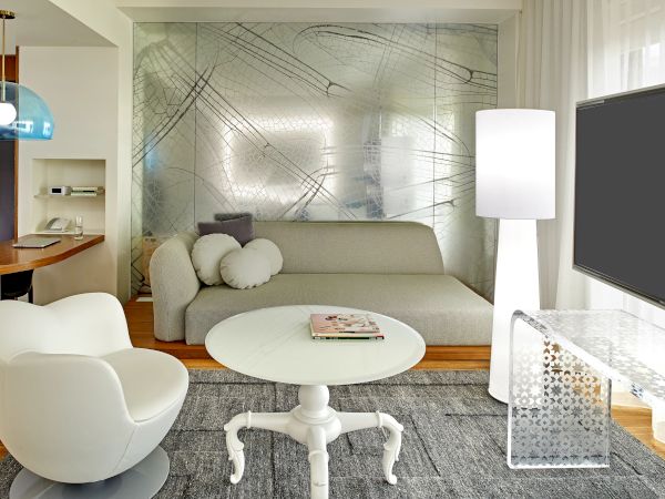 A modern living room with a white curved chair, round white coffee table, gray sofa, floor lamp, and a wall-mounted TV; stylish, airy space.