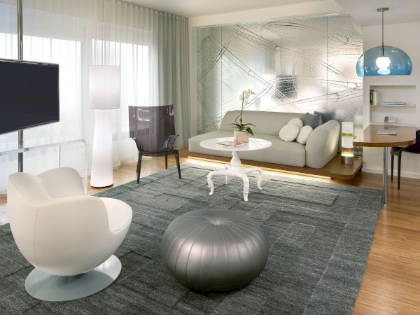 Modern living room with gray rug, white chairs, love seat, glass partition, flat-screen TV, and a large blue pendant light, stylish and airy.
