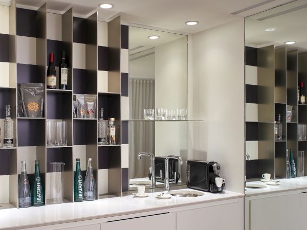 A modern bar/kitchen setup with a black-and-white checker shelf, bottles, glassware, and a clean white counter under bright lighting.