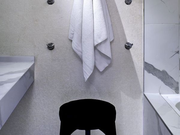 A white towel hangs on hooks above a glossy black stool in a modern bathroom with a marble wall and checkerboard floor.