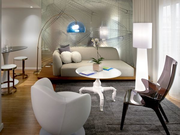 A modern, open-concept living room with a glass wall, stylish seating including white and black chairs, a round coffee table, and a blue pendant light.