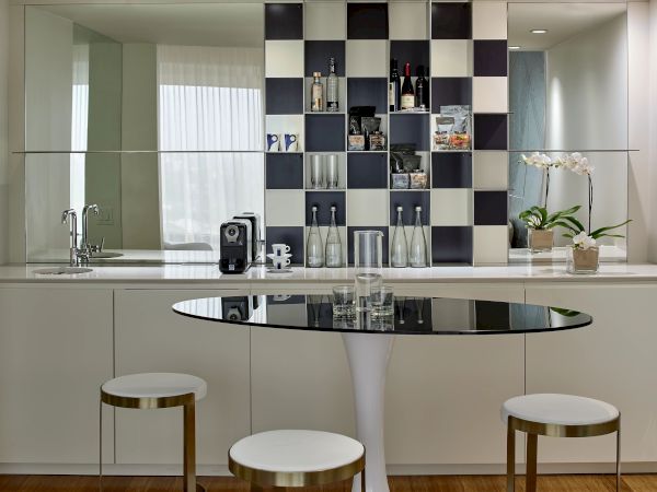 A modern kitchen with a glossy black-and-white checkered wall, open shelving, a round black glass table, and three white stools by a light counter.