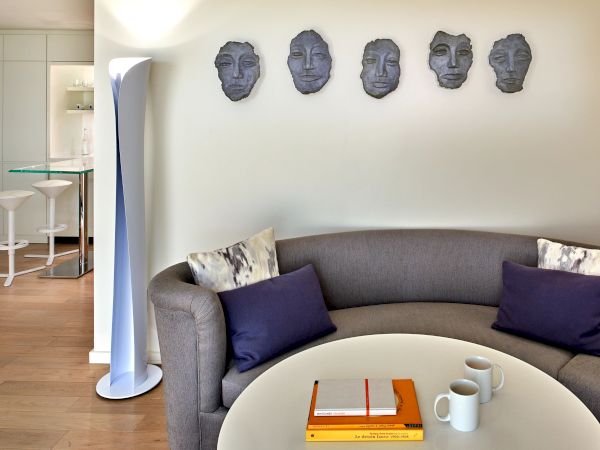 Living room with a curved gray sofa, purple accent pillows, a round coffee table, and wall-mounted metal masks above the sofa, ending the sentence.