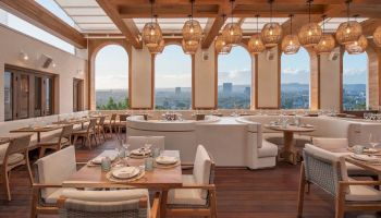 A stylish rooftop restaurant with wooden beams, warm hanging lanterns, cushioned seating, and panoramic city views; chic casual dining space.