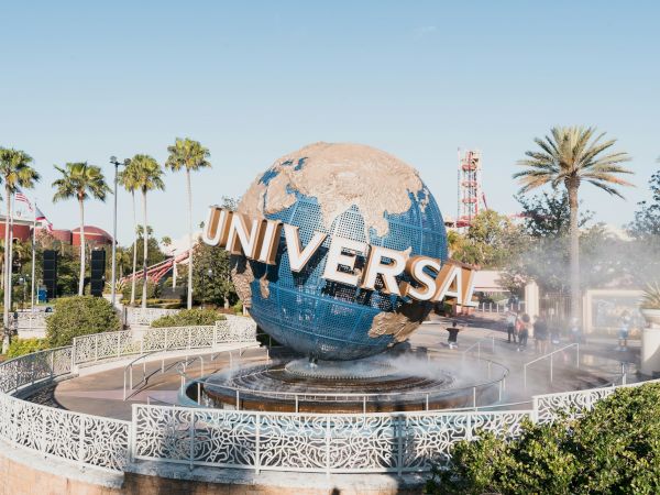A large globe fountain at Universal Studios, with spray, palm trees, and a decorative railing around the display. Universal sign atop the globe.