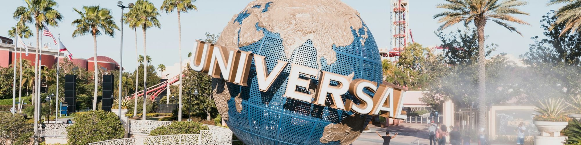 A large globe sculpture labeled &ldquo;UNIVERSAL&rdquo; sits in a circular fountain, surrounded by palm trees and a sunny park backdrop.