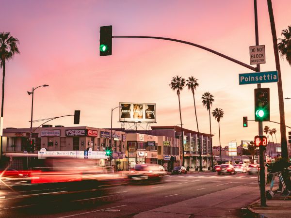 A busy street scene at dusk with palm trees, traffic, and neon signs along a crossroad near Ponsettia Street, city vibe.