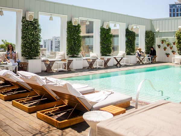 A sunny rooftop pool scene with lounge chairs, a clear blue pool, and stylish seating under a bright sky.