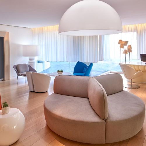 A modern, bright living room with curved beige seating, white pendant light, soft blue accents, and glossy white furniture, airy and inviting.