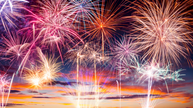 Colorful fireworks exploding above a sunset sky, bright trails and bursts lighting up the night.