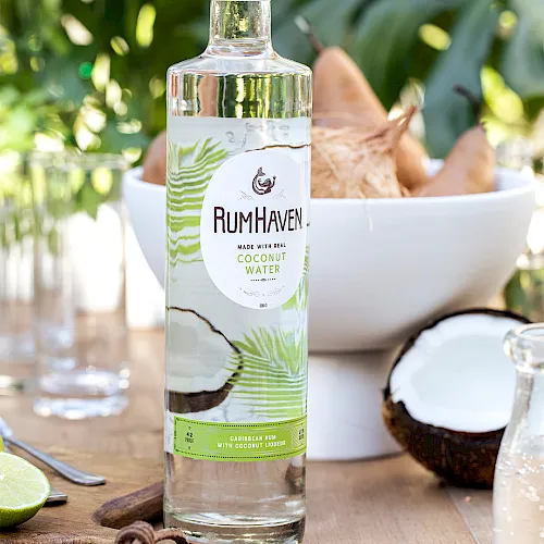A RumHaven bottle labeled “Made with real coconut water,” with tropical drink ingredients on a sunny outdoor table.