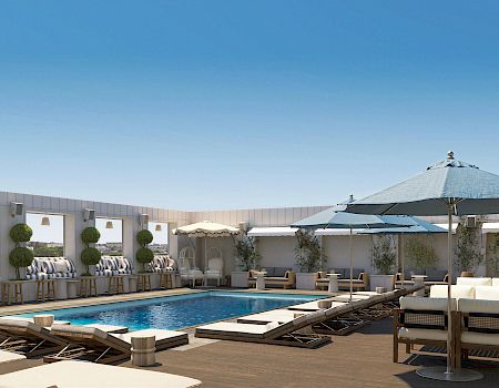 A sunny rooftop pool terrace with blue water, striped loungers, and several canopy umbrellas under a clear sky.