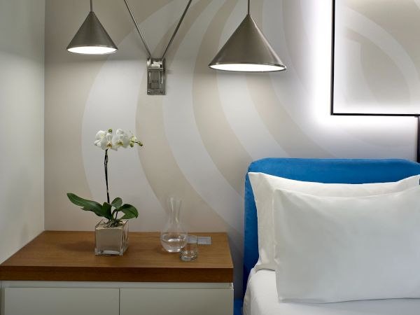 A modern room with two metal ceiling lamps, a blue chair, an orchid on a wooden table, and wall-striped decor behind it.