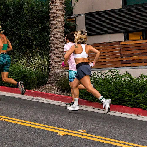 Three runners sprint on an outdoor track beside a stone pillar and greenery.